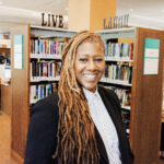 A smiling woman stands in front of library bookshelves