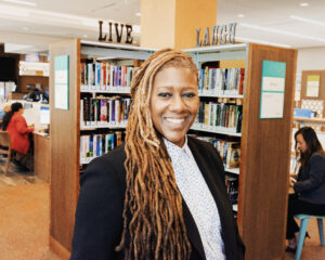 A smiling woman stands in front of library bookshelves